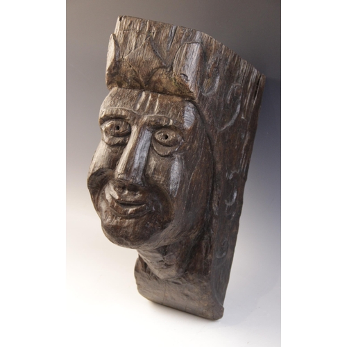 467 - An early 16th century naïve carved oak figural corbel, carved with a smiling face, within a scroll c... 