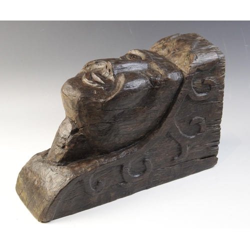 467 - An early 16th century naïve carved oak figural corbel, carved with a smiling face, within a scroll c... 