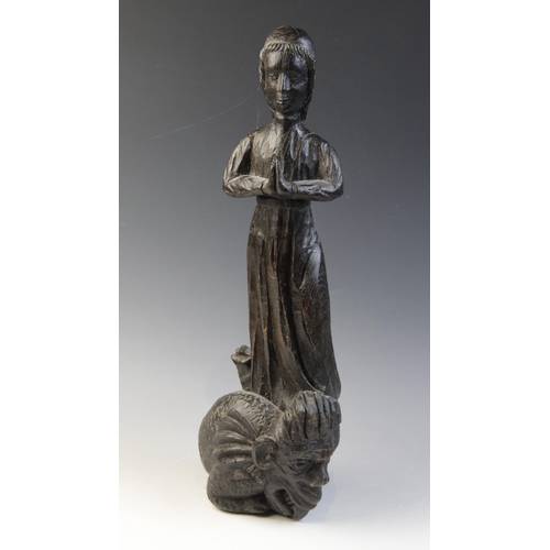 479 - An oak carved figure of a maiden at prayer, standing upon a grotesque scaly creature, with mask and ... 