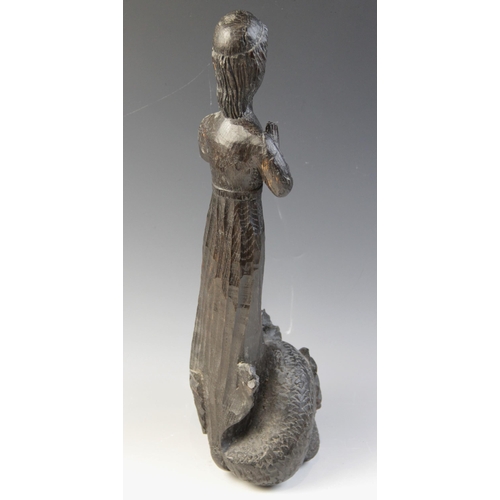 479 - An oak carved figure of a maiden at prayer, standing upon a grotesque scaly creature, with mask and ... 