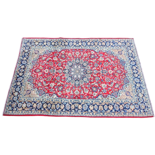 275 - * A large Iranian wool rug, with a traditional blue medallion radiating trailing foliage upon a red ... 