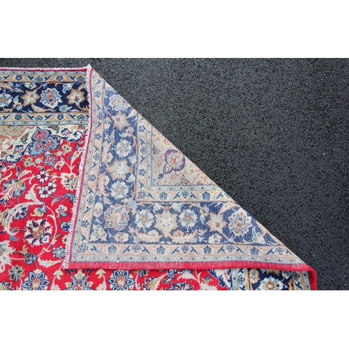 275 - * A large Iranian wool rug, with a traditional blue medallion radiating trailing foliage upon a red ... 