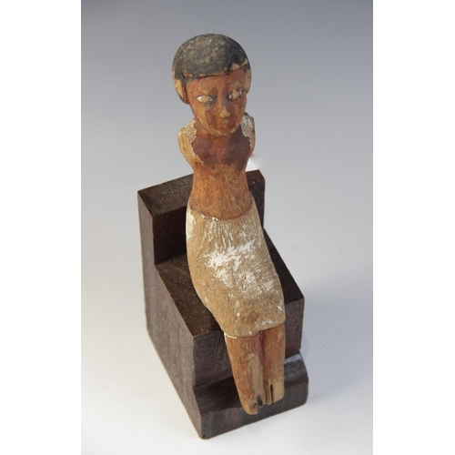 131 - An Egyptian polychrome painted wood model figure, shown seated with arms missing, wearing a short wi... 