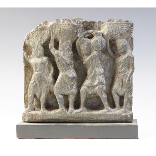 136 - A schist relief, carved in high relief with four tunic-clad figures, three carrying a basket on thei... 