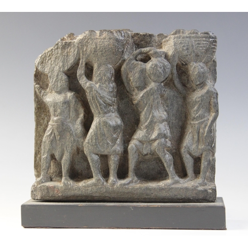 136 - A schist relief, carved in high relief with four tunic-clad figures, three carrying a basket on thei... 