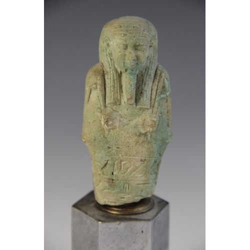 160 - A fragmentary Egyptian green glazed faience shabti, holding a pick and hoe with the remains of two h... 