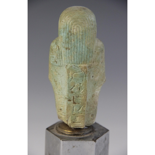 160 - A fragmentary Egyptian green glazed faience shabti, holding a pick and hoe with the remains of two h... 