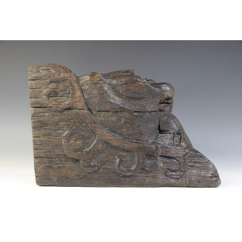 467 - An early 16th century naïve carved oak figural corbel, carved with a smiling face, within a scroll c... 