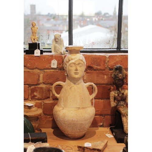 108 - A terracotta water jug, the amphora form jug with loop handles, the neck modelled as a head with fla... 