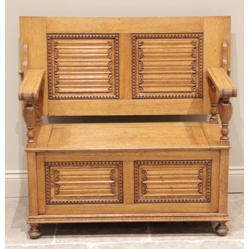 728 - An early 20th century golden oak monks bench, the 'up and over' back panel carved with linen fold de... 