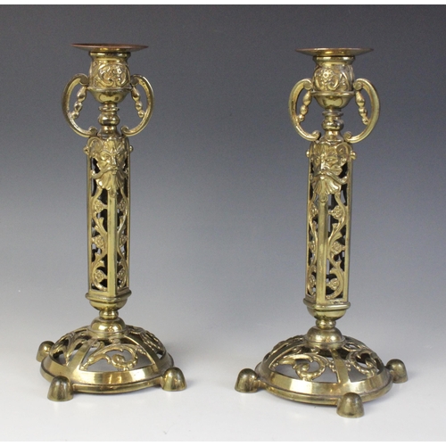 610 - A pair of Victorian brass candlesticks, each cast with arabesques and masks above a domed and pierce... 