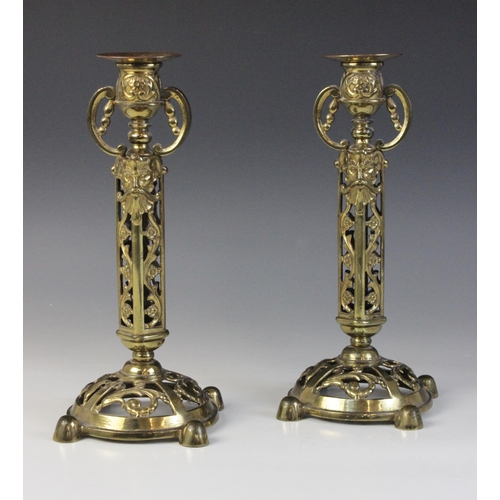 610 - A pair of Victorian brass candlesticks, each cast with arabesques and masks above a domed and pierce... 