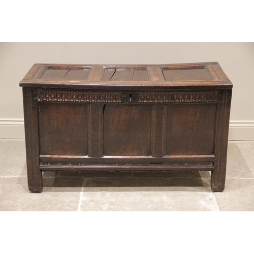 712 - An early 18th century oak coffer, the three panel hinged top, above a nulled frieze and three confor... 