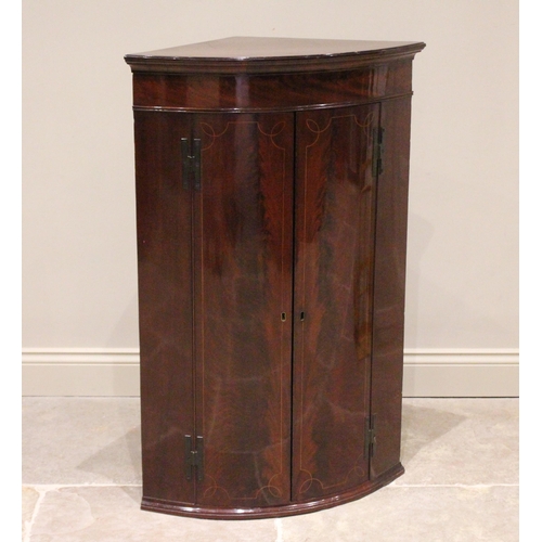 731 - A George III mahogany bow front hanging corner cupboard, the pair of flame mahogany doors opening to... 