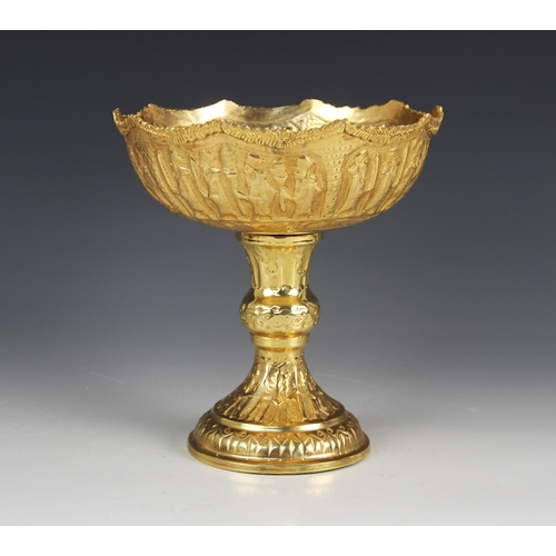 68 - A gold coloured pedestal dish, the circular bowl embossed with a continuous frieze of figures in pro... 