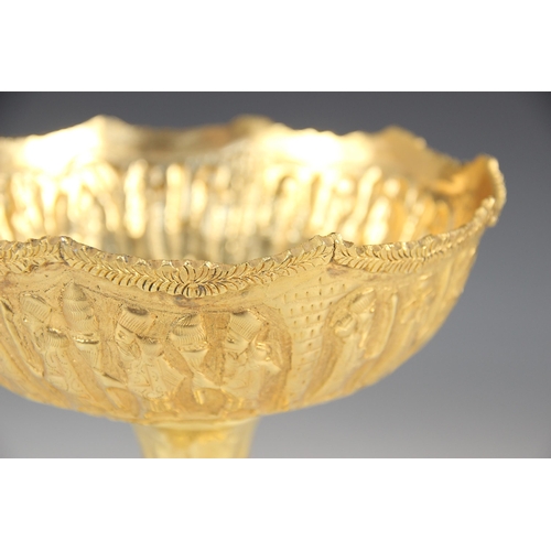 68 - A gold coloured pedestal dish, the circular bowl embossed with a continuous frieze of figures in pro... 