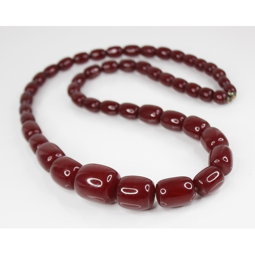 74 - A cherry amber bead necklace, comprising forty-nine barrel shaped beads, measuring between 11mm x 9m... 