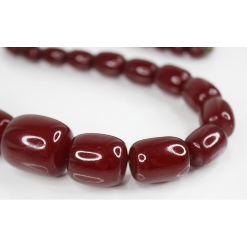 74 - A cherry amber bead necklace, comprising forty-nine barrel shaped beads, measuring between 11mm x 9m... 