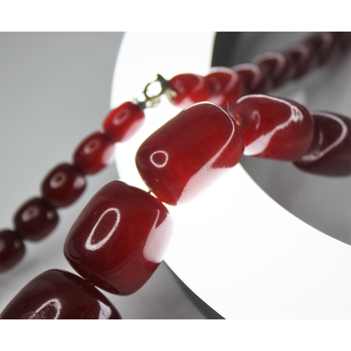 74 - A cherry amber bead necklace, comprising forty-nine barrel shaped beads, measuring between 11mm x 9m... 