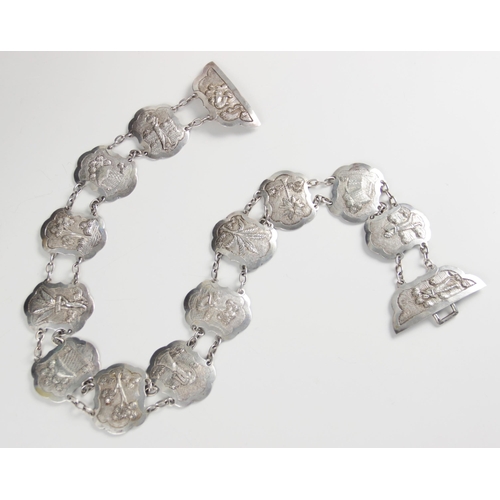 25 - An Asian silver coloured belt, each lozenge shaped link with scalloped borders, embossed with rural ... 