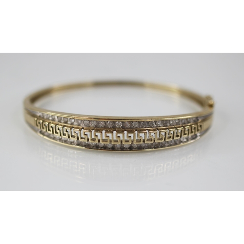 109 - A 9ct gold diamond set hinged bangle, the central channel designed as a pierced greek key border fla... 