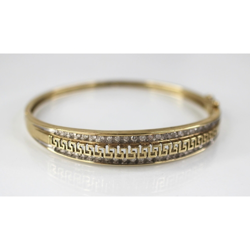 109 - A 9ct gold diamond set hinged bangle, the central channel designed as a pierced greek key border fla... 