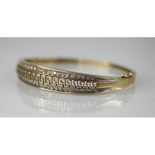 109 - A 9ct gold diamond set hinged bangle, the central channel designed as a pierced greek key border fla... 