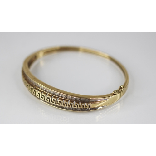 109 - A 9ct gold diamond set hinged bangle, the central channel designed as a pierced greek key border fla... 