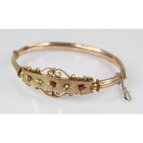 124 - An Edwardian 9ct gold ruby and diamond set hinged bangle, designed as three mixed cut rubies and two... 