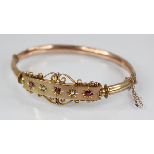 124 - An Edwardian 9ct gold ruby and diamond set hinged bangle, designed as three mixed cut rubies and two... 