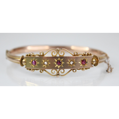 124 - An Edwardian 9ct gold ruby and diamond set hinged bangle, designed as three mixed cut rubies and two... 