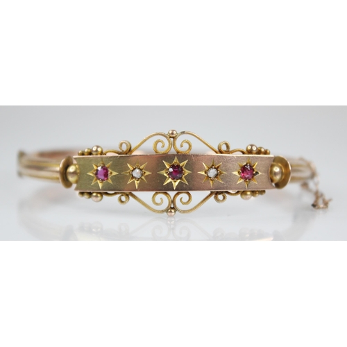 124 - An Edwardian 9ct gold ruby and diamond set hinged bangle, designed as three mixed cut rubies and two... 