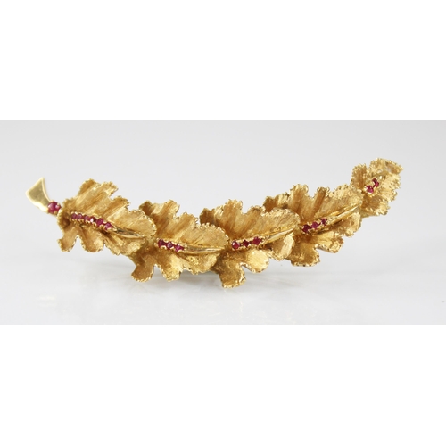 134 - A continental 18ct gold ruby set brooch, modelled as a curved band of five textured oak leaves set w... 