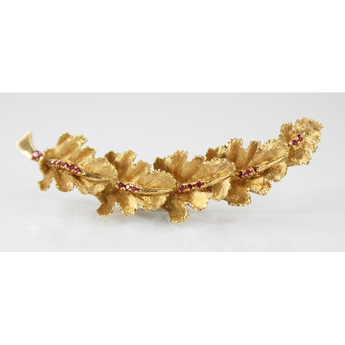 134 - A continental 18ct gold ruby set brooch, modelled as a curved band of five textured oak leaves set w... 