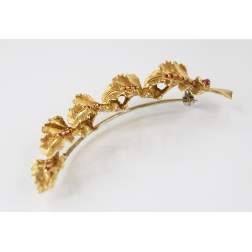 134 - A continental 18ct gold ruby set brooch, modelled as a curved band of five textured oak leaves set w... 