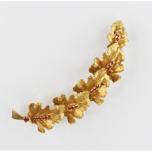 134 - A continental 18ct gold ruby set brooch, modelled as a curved band of five textured oak leaves set w... 