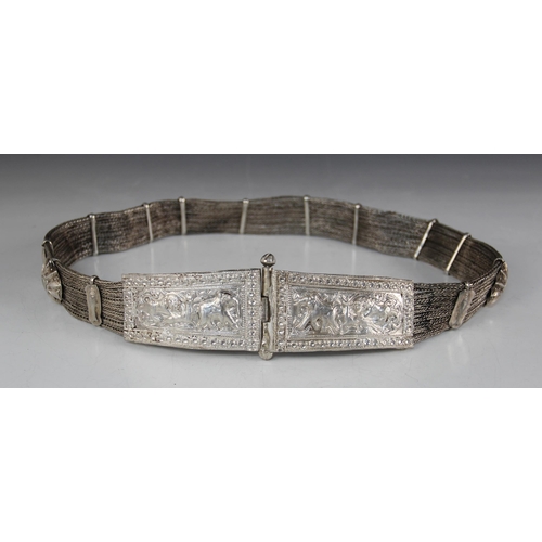20 - An Indian silver coloured belt, designed as two tapered rectangular buckles, ornately embossed with ... 