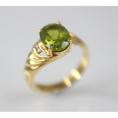 77 - A peridot and diamond 18ct gold ring, the central oval mixed cut peridot measuring 10mm x 8mm, claw ... 