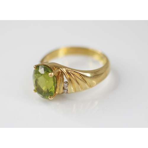 77 - A peridot and diamond 18ct gold ring, the central oval mixed cut peridot measuring 10mm x 8mm, claw ... 