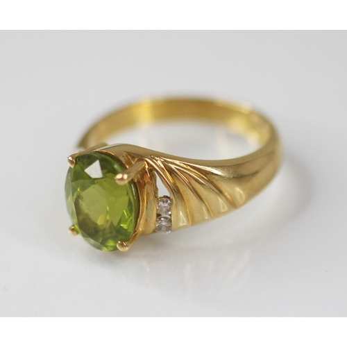 77 - A peridot and diamond 18ct gold ring, the central oval mixed cut peridot measuring 10mm x 8mm, claw ... 