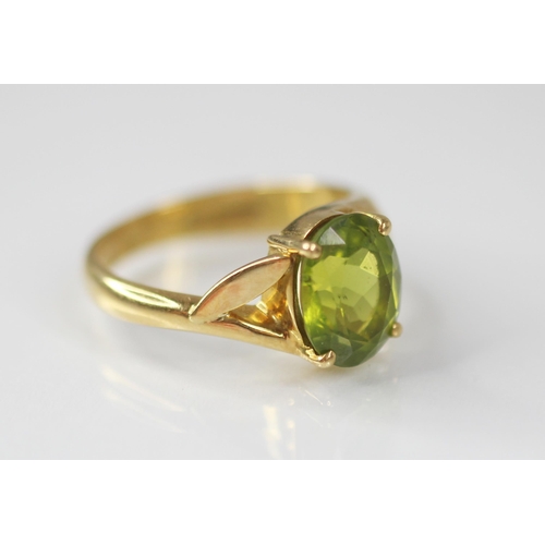 77 - A peridot and diamond 18ct gold ring, the central oval mixed cut peridot measuring 10mm x 8mm, claw ... 