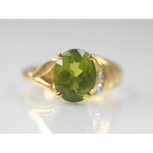 77 - A peridot and diamond 18ct gold ring, the central oval mixed cut peridot measuring 10mm x 8mm, claw ... 