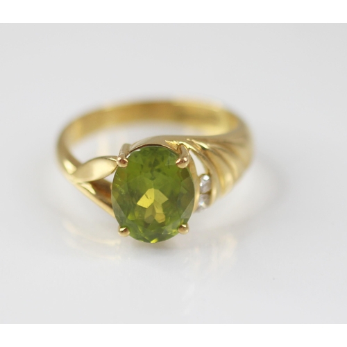 77 - A peridot and diamond 18ct gold ring, the central oval mixed cut peridot measuring 10mm x 8mm, claw ... 