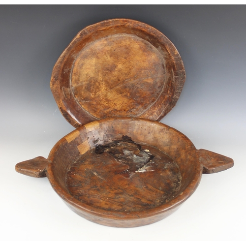 183 - A carved elm twin handled dish, early 19th century, of wide flat-bottomed form, showing later repair... 