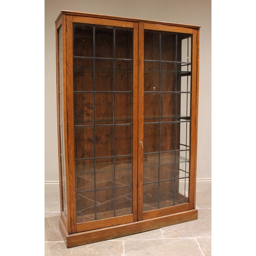 828 - An early 20th century oak and leaded glass display cabinet, the twin doors opening to three later gl... 