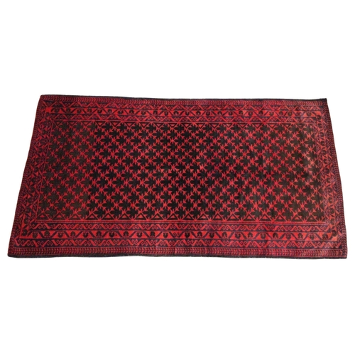 613 - An Afghan Belouch wool rug, in deep red and blue colourways, the central field with a lattice design... 