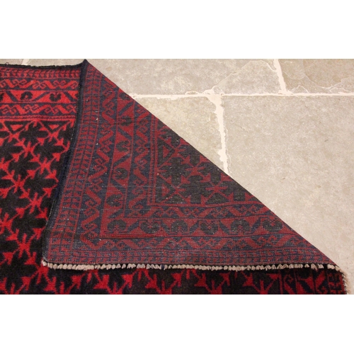 613 - An Afghan Belouch wool rug, in deep red and blue colourways, the central field with a lattice design... 