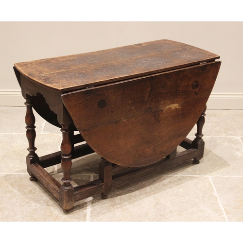 712 - An 18th century oak drop leaf table, the oval top above a shaped frieze upon baluster and inverted b... 