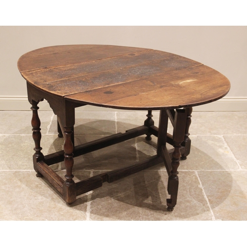 712 - An 18th century oak drop leaf table, the oval top above a shaped frieze upon baluster and inverted b... 