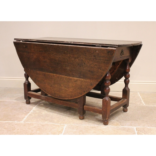 723 - An 18th century oak drop leaf dining table, the oval plank top above a single frieze drawer, upon bo... 